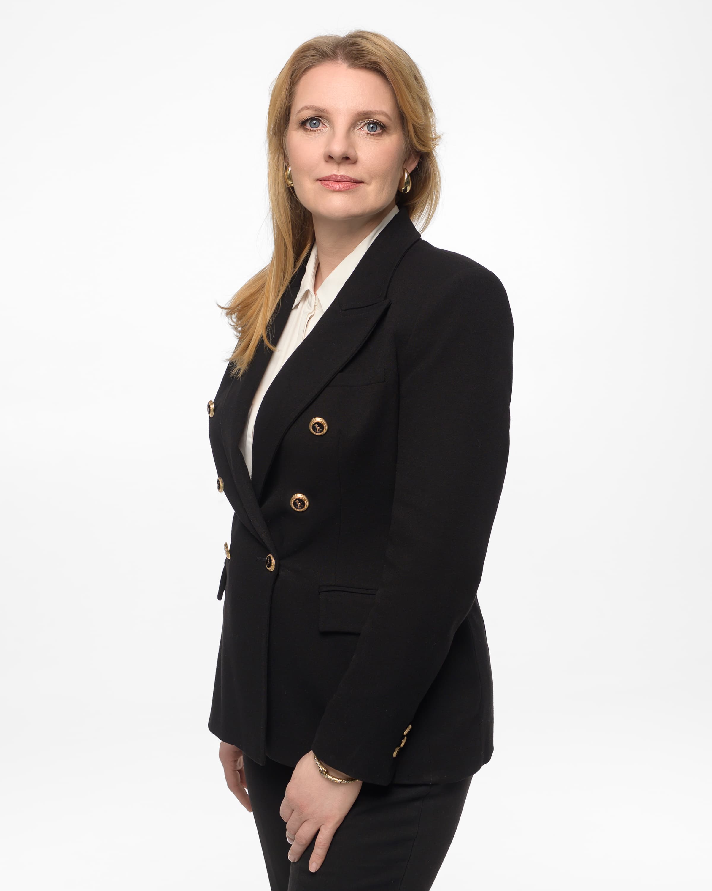 Blonde woman in a black double-breasted blazer with gold buttons against a white background.